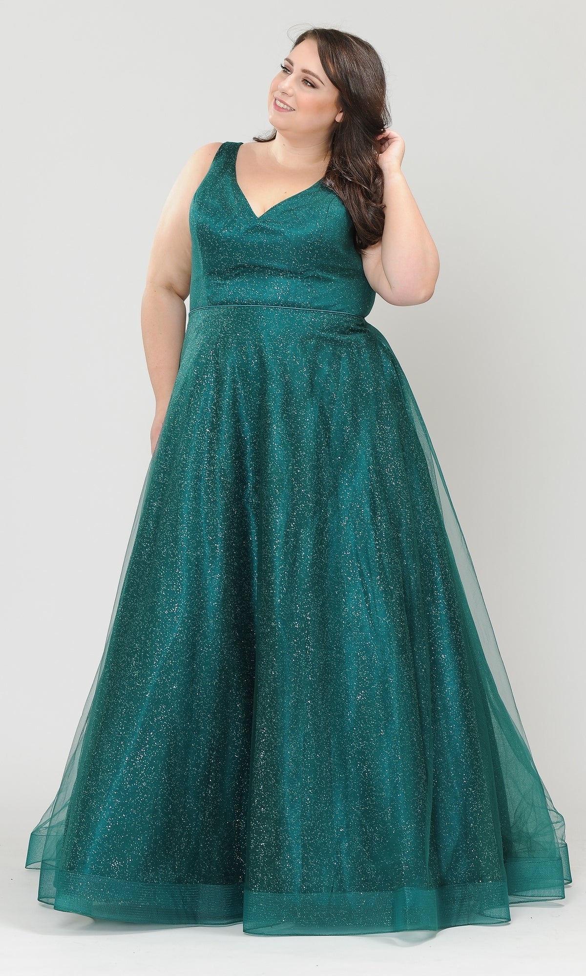 A woman stands against a plain light background wearing the Glitter-Tulle Plus-Size Long Prom Gown W1024, a floor-length, sleeveless emerald green A-line dress with a V-neckline and sparkly tulle fabric.